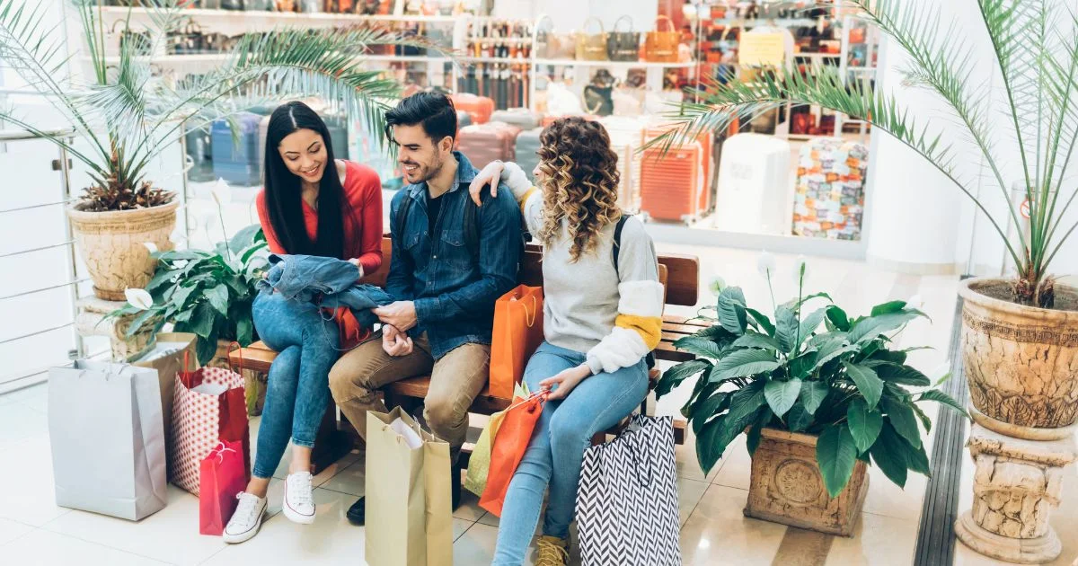 Three friends sitting on a bench with shopping bags in a mall